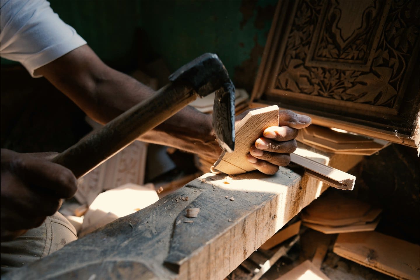 Artigiano che intaglia dettagli intricati in legno chiaro con uno strumento.