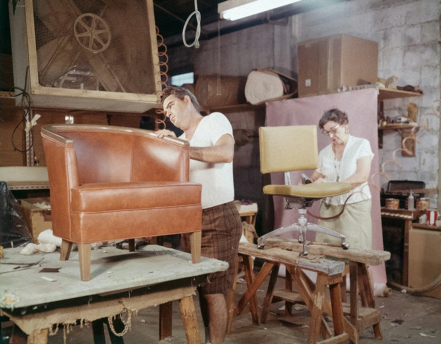 Due artigiani lavorano su sedie imbottite all'interno di un laboratorio rustico.